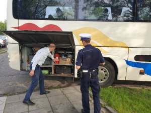 Kontrola autokaru przez policjanta ruchu drogowego na parkingu przed budynkiem Policji