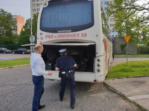 Kontrola autokaru przez policjanta ruchu drogowego na parkingu przed budynkiem Policji