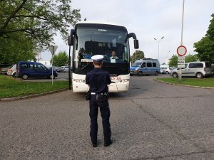 Kontrola autokaru przez policjanta ruchu drogowego na parkingu przed budynkiem Policji