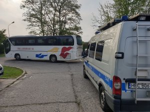 Kontrola autokaru przez policjanta ruchu drogowego na parkingu przed budynkiem Policji