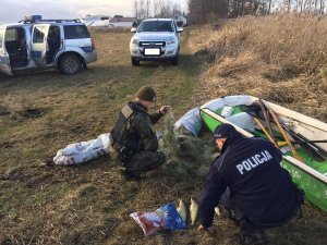 policjant i funkcjonariusz PSR przeglądają narzędzia kłusownika i złowione ryby