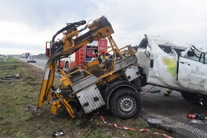 Policjanci ruchu drogowego zabezpieczający miejsce wypadku na autostradzie. Na zdjęciu znajduje się uszkodzony pojazd mitsubishi na pierwszym planie. Na drugim widoczny jest radiowóz policyjny oraz wóz strażacki