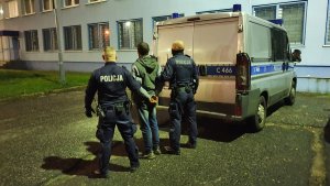 Zdjęcie policjantów z zatrzymanym mężczyzną do usiłowania zabójstwa obok radiowozu zgodnie z treścią informacji