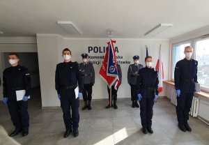 Ślubowanie policjantów w pomieszczeniu komendy policji. Na przodzie czterej nowi policjanci a w tle poczet sztandarowy.