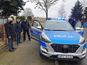 Przekazanie radiowozu. Na środku zdjęcia radiowóz w kolorze srebrnym i niebieskim marki hyundai Tucson. Po prawej stronie policjant umundurowany z Posterunku Policji w Izbicy Kujawskiej, po lewej trzy postacie wśród których jest Burmistrz i Przewodniczący Rady Izbicy Kujawskiej