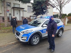 Przekazanie radiowozu. Na środku zdjęcia radiowóz w kolorze srebrnym i niebieskim marki hyundai Tucson. Po prawej stronie policjant umundurowany z Posterunku Policji w Izbicy Kujawskiej, po lewej trzy postacie wśród których jest Burmistrz i Przewodniczący Rady Izbicy Kujawskiej