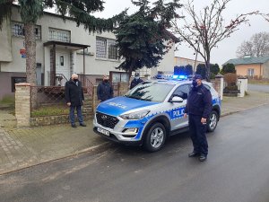 Przekazanie radiowozu. Na środku zdjęcia radiowóz w kolorze srebrnym i niebieskim marki hyundai Tucson. Po prawej stronie policjant umundurowany z Posterunku Policji w Izbicy Kujawskiej, po lewej trzy postacie wśród których jest Burmistrz i Przewodniczący Rady Izbicy Kujawskiej