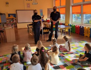 Policjanci omawiają z przedszkolakami zasady bezpieczeństwa w ruchu drogowym w klasie.