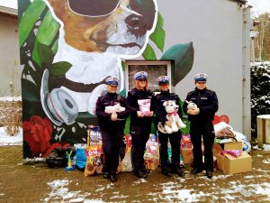 Na tle ściany z pomalowanym psem i stojącymi podarunkami stoją cztery policjantki umundurowane