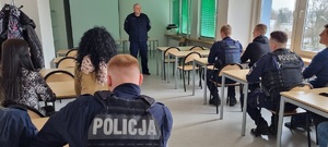 Spotkanie w sali komendy. Na pierwszym planie policjanci siedzący tyłem. W głębi zdjęcia policjant stojący.