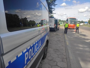 Zdjęcie podczas działań kontrolnych. Po lewej radiowóz policyjny i Inspekcji Transportu Drogowego, Po prawej policjanci stojący tyłem i kontrolowany autokar