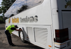 Policjant przeprowadza kontrolę autobusu, sprawdza oponę