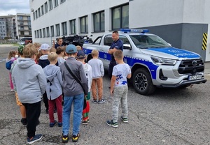 grupa dzieci stoi przy policjantce i policjancie obok radiowozu