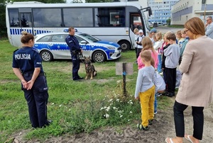 grupa dzieci patrzy na policjanta i towarzyszącego mu psa służbowego