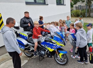 grupa dzieci stoi przy policyjnym motocyklu, jedno dziecko siedzi na tym motocyklu