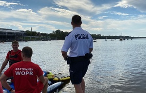 policjant i ratownik WOPR patrzą na płynące po rzece łodzie