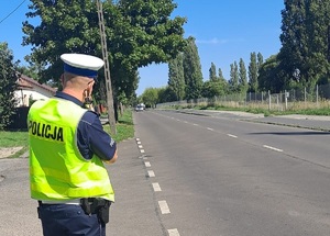 policjant patrzy na jadące drogą auto i mierzy prędkość