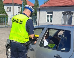 policjant stoi przy aucie i sprawdza urządzeniem trzeźwość kierowcy