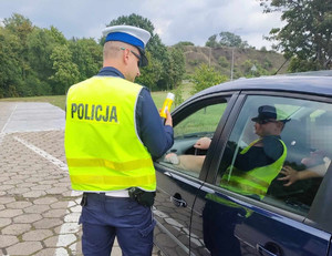 Policjant podczas kontroli trzeźwości stojący przy pojeździe tyłem z widocznym napisem Policja