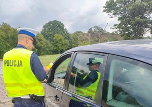 Policjant podczas kontroli trzeźwości stojący przy pojeździe tyłem z widocznym napisem Policja