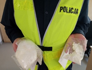 policjant trzyma w rękach dwa woreczki z białym proszkiem