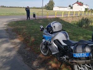 policjant stoi przy drodze i trzymanym w ręku urządzeniem mierzy prędkość pojazdów