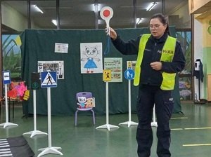 Policjantka podczas pogadanki z przedszkolakami prezentuje znaki drogowe i policyjną tarczę do zatrzymywania