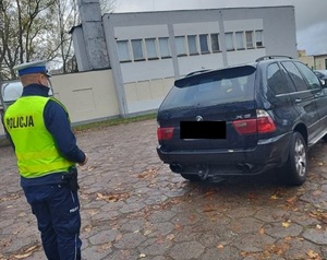 Policjant podczas kontroli drogowej. Stoi tyłem i sprawdza oświetlenie pojazdu z tyłu