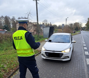 Policjant podczas kontroli drogowej. Stoi tyłem i sprawdza oświetlenie pojazdu z przodu