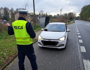 Policjant podczas kontroli drogowej. Stoi tyłem i sprawdza oświetlenie pojazdu z przodu