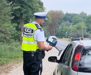 policjanci ruchu drogowego w kamizelkach z napisem POLICJA stoją przy drodze i kontrolują kierujących autami